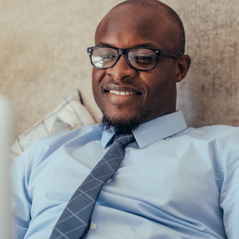 Reclining and smiling dark-skinned man with tie and glasses